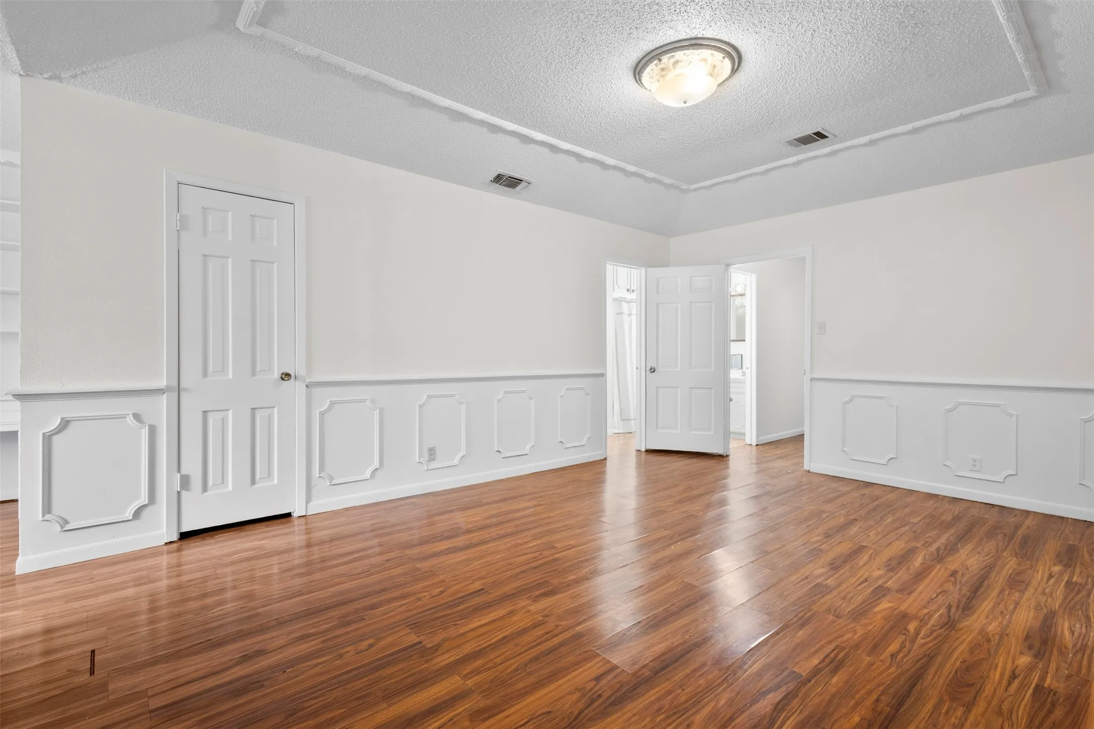 Unfurnished bedroom featuring a wainscoted wall, a decorative wall, dark wood-type flooring, and a textured ceiling