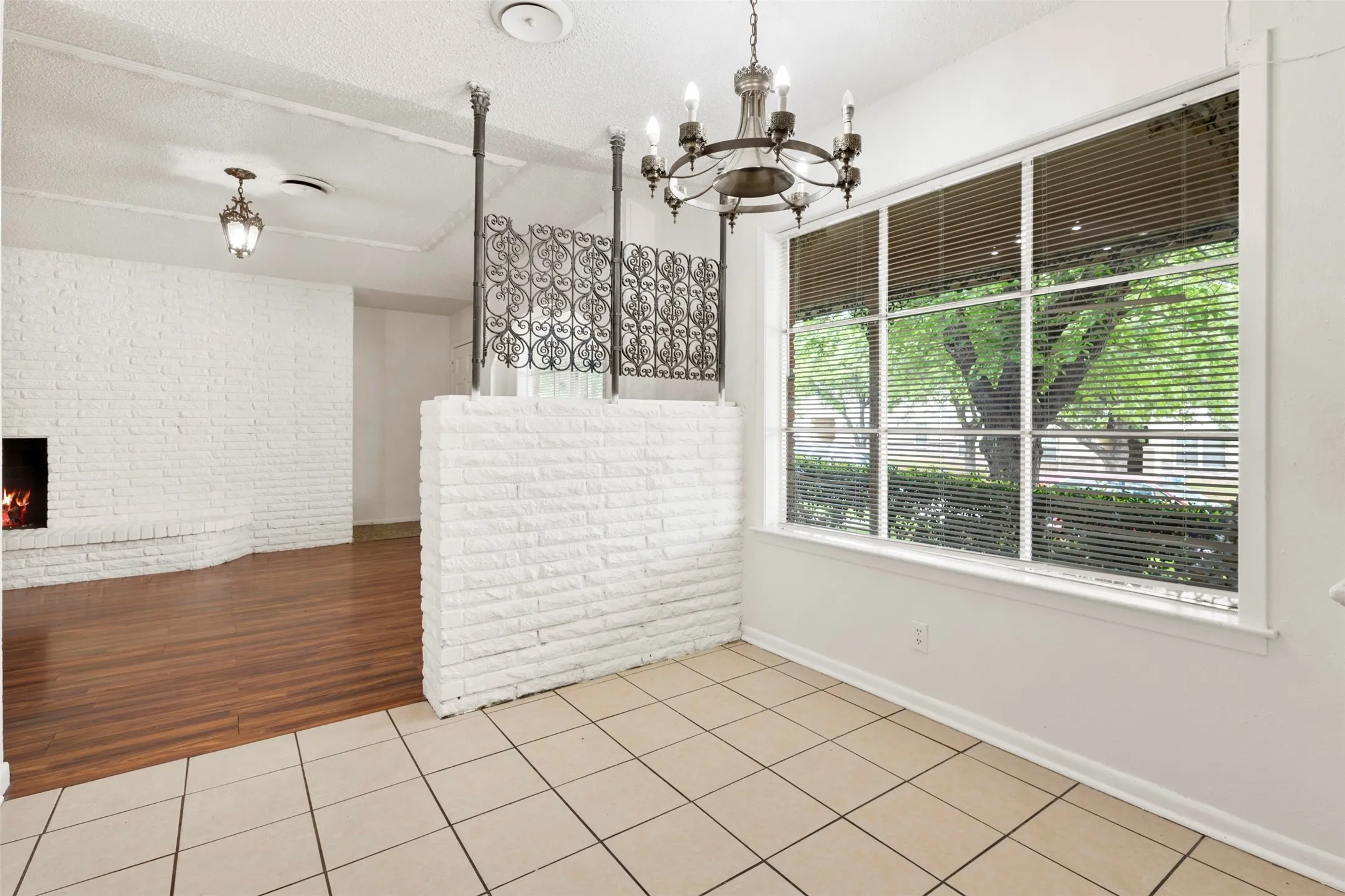 Unfurnished dining area featuring brick wall, light tile patterned floors, suspended lighting, a fireplace, and a textured ceiling