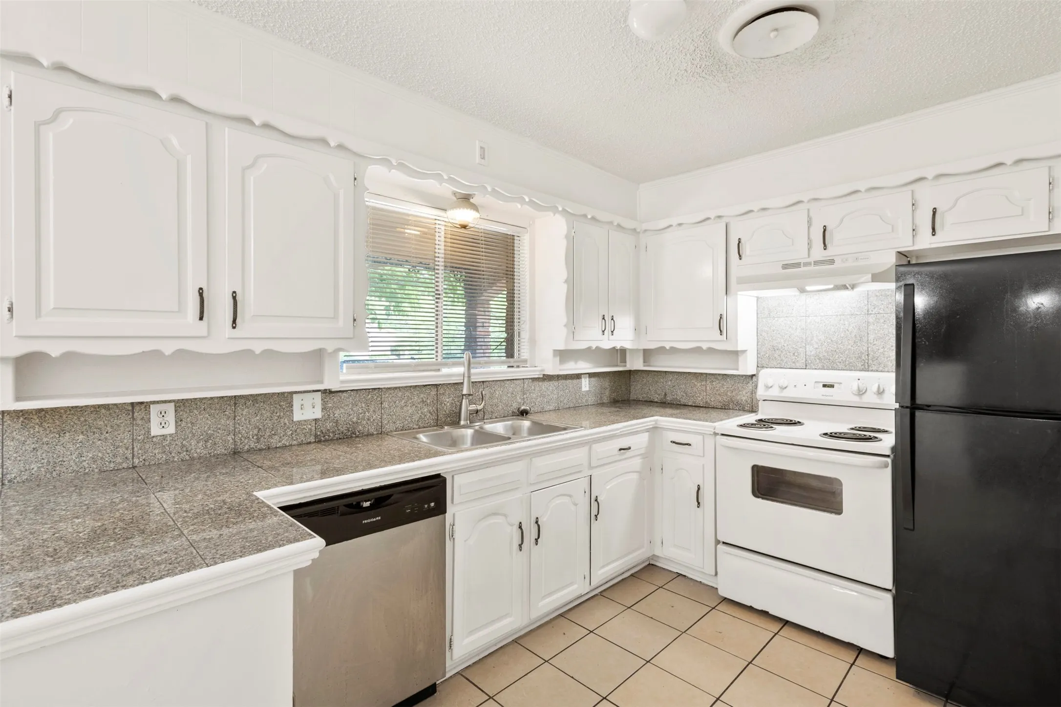 Kitchen featuring electric range, freestanding refrigerator, tile countertops, dishwasher, and light tile patterned flooring