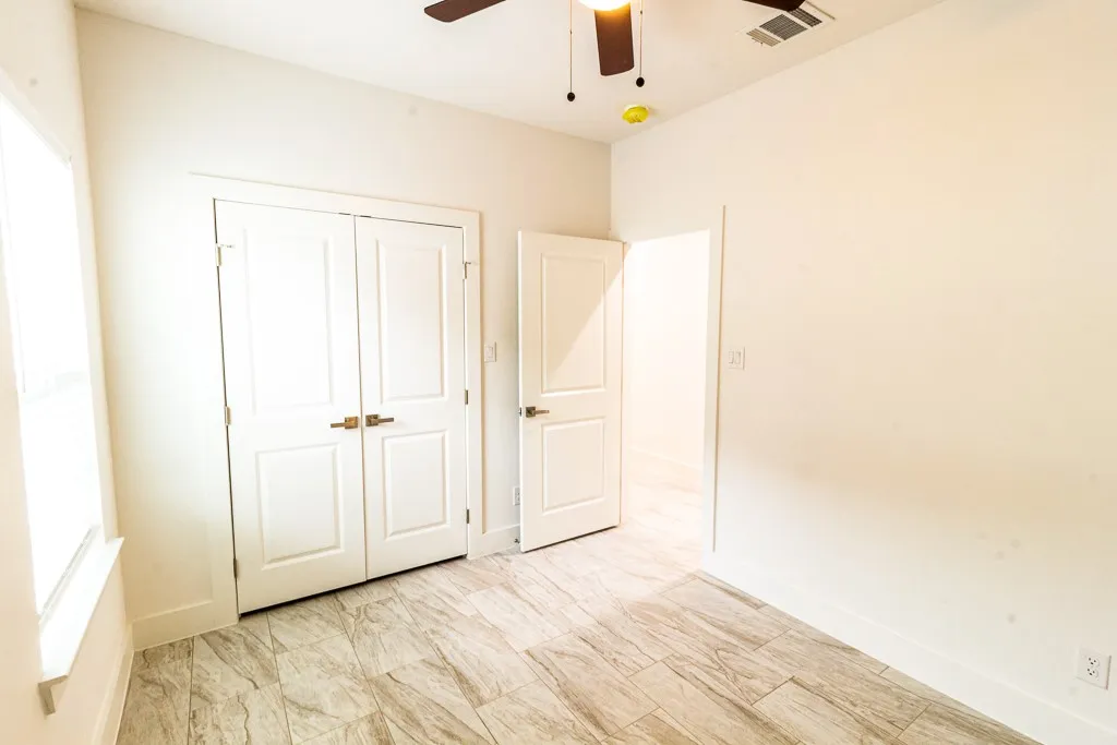 Tile flooring, white bi-fold doors, white interior doors, window with white trim, and ceiling fan with light fixture
