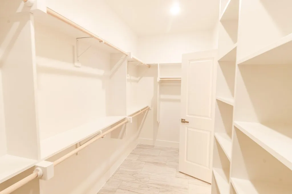 Spacious walk-in closet featuring extensive built-in shelving and hanging rods throughout, wood-finish flooring, and bright recessed lighting for optimal visibility and storage organization