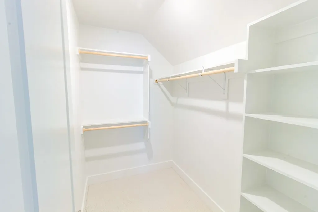 Walk-in closet with built-in shelving, dual hanging rods, and light-colored carpeting