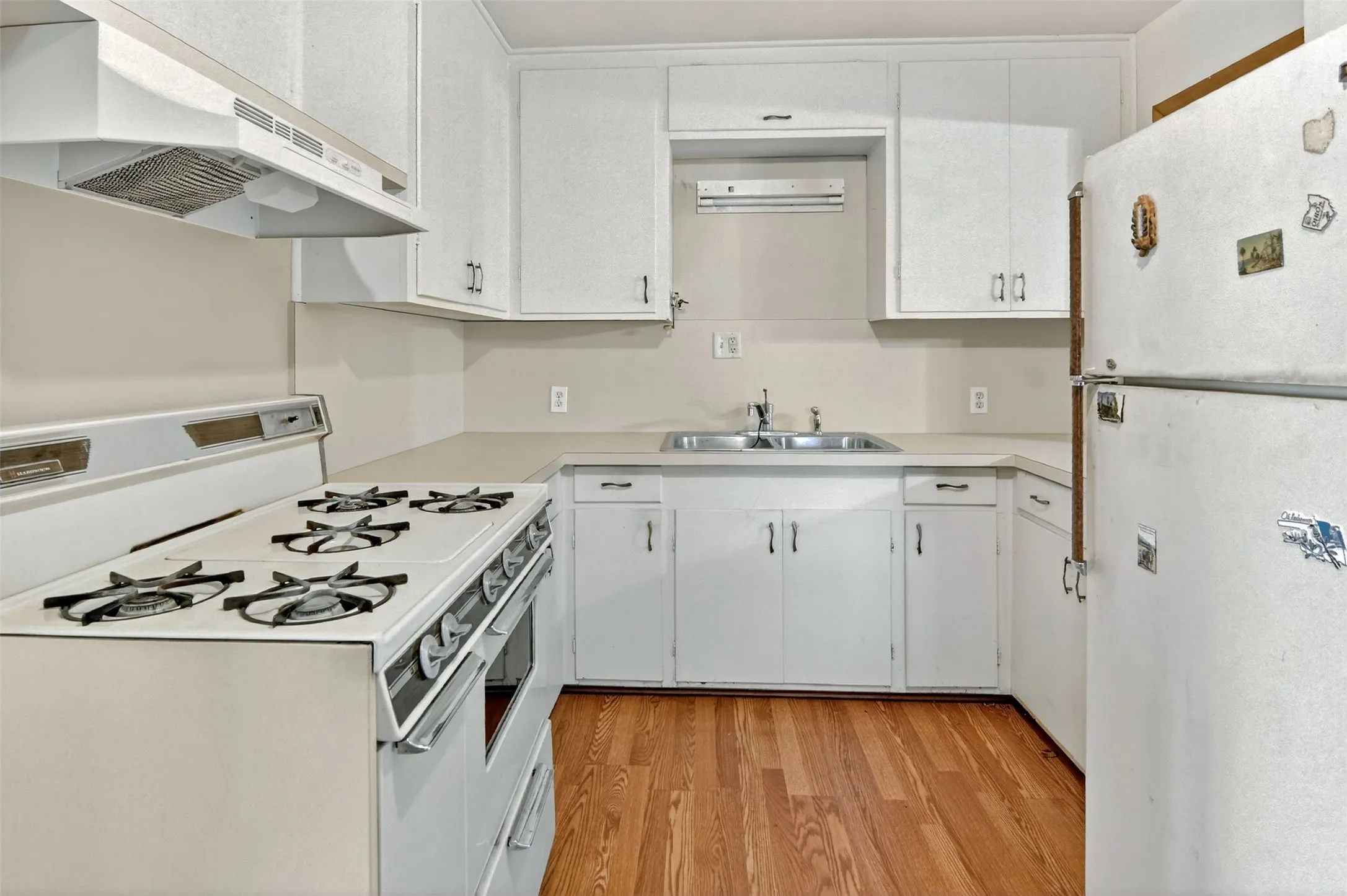 Kitchen featuring white appliances, light countertops, white cabinetry, and light wood-style floors.