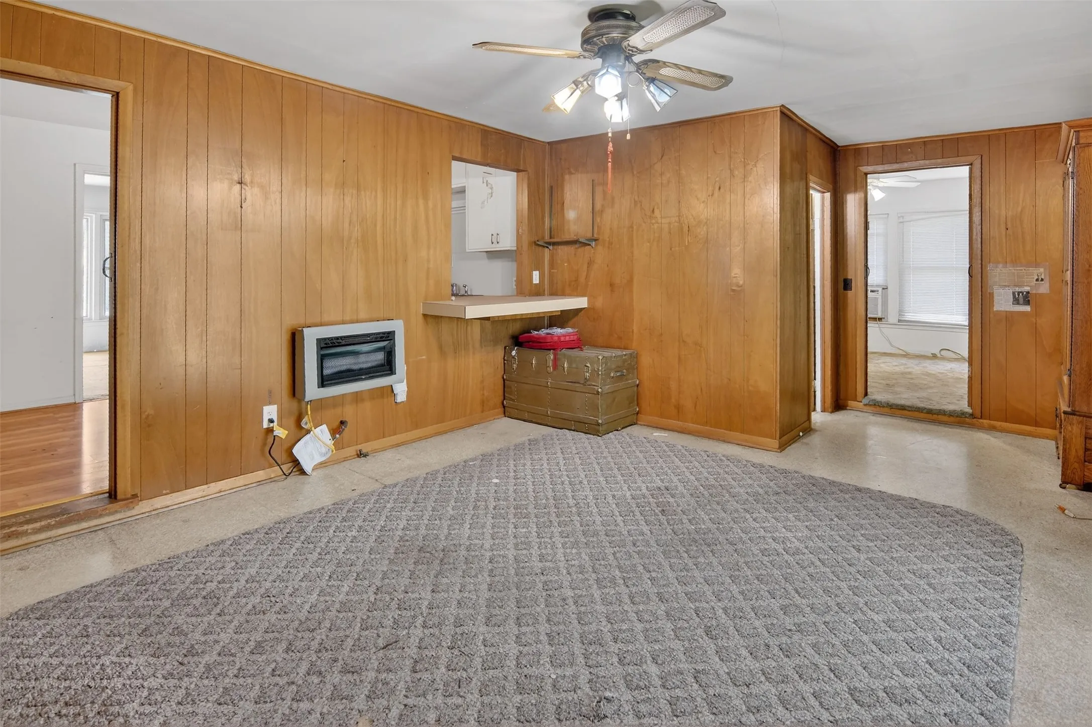 Den features paneling on walls, a ceiling fan, and a heating unit.
