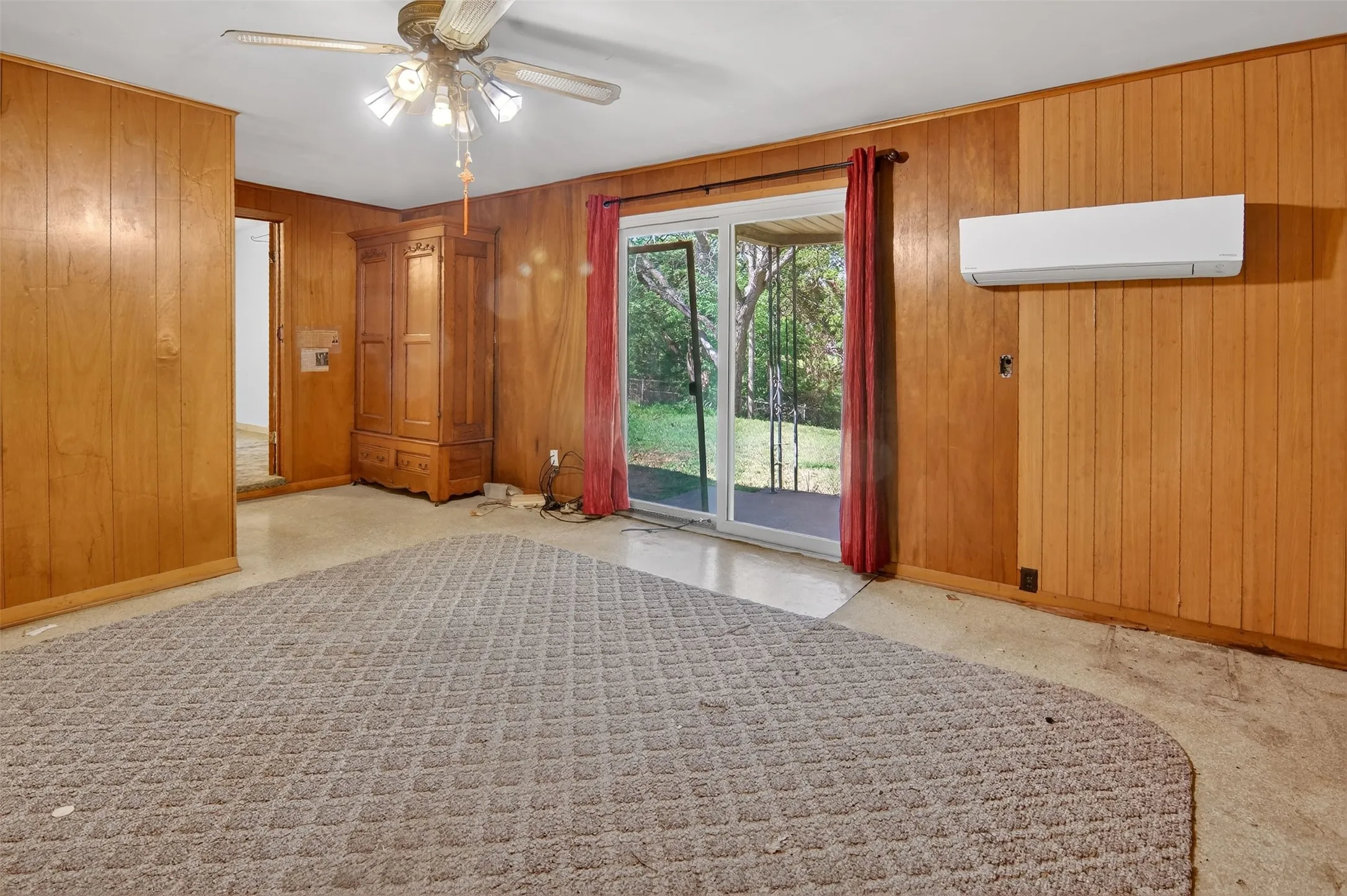 Den with ceiling fan, wood panelling, carpet,  and sliding glass door to large backyard.