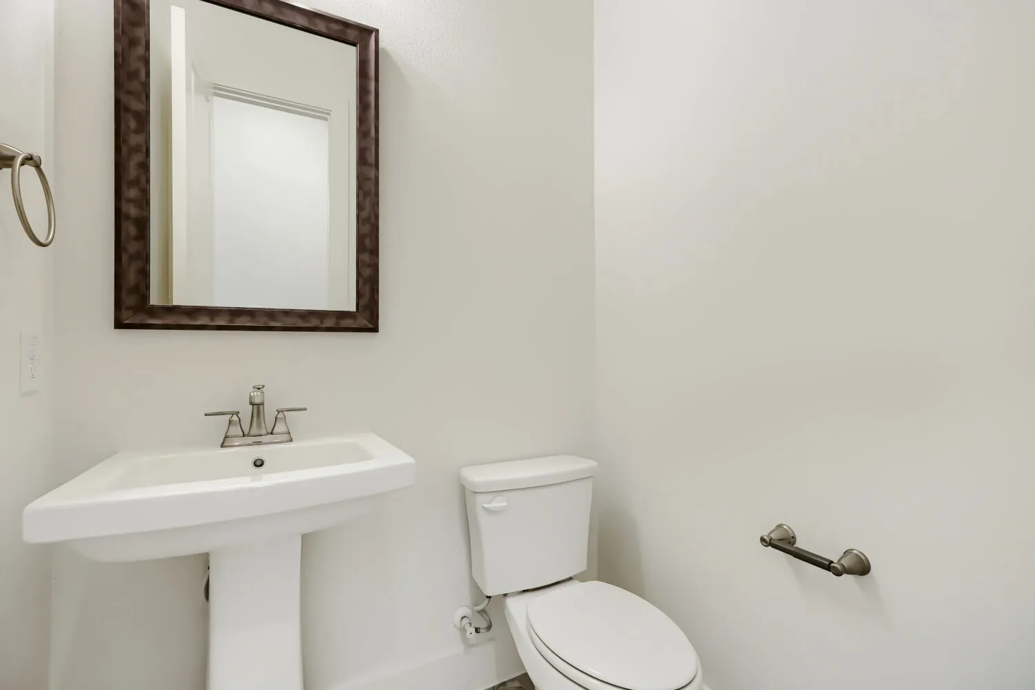 Pedestal sink with chrome faucet, framed mirror, and white wall finishes