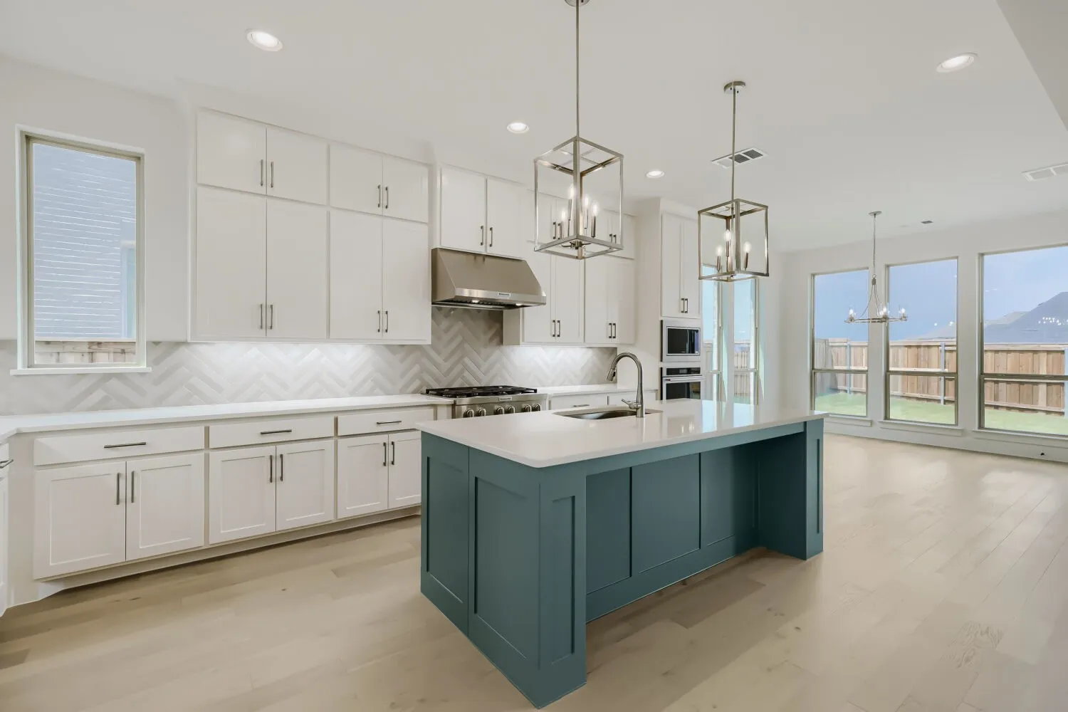 Modern kitchen featuring an expansive center island with a light-toned countertop and teal-painted cabinetry