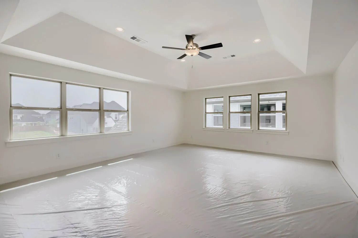 Spacious room featuring multiple large windows, a tray ceiling, recessed lighting, and a ceiling fan
