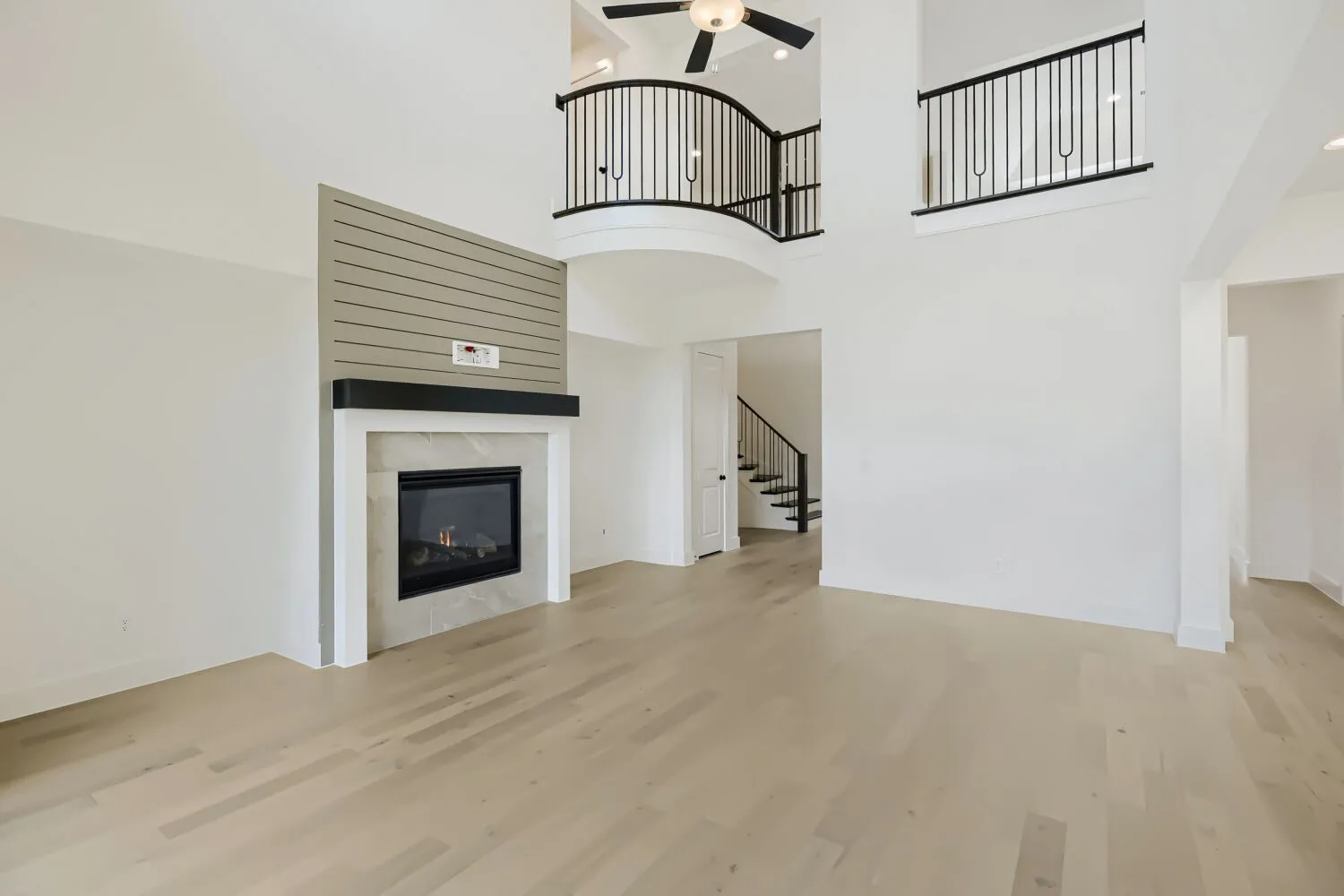 Two-story living area featuring light wood-finish flooring and a fireplace with a white mantel, stone-look surround, and shiplap-style accent wall