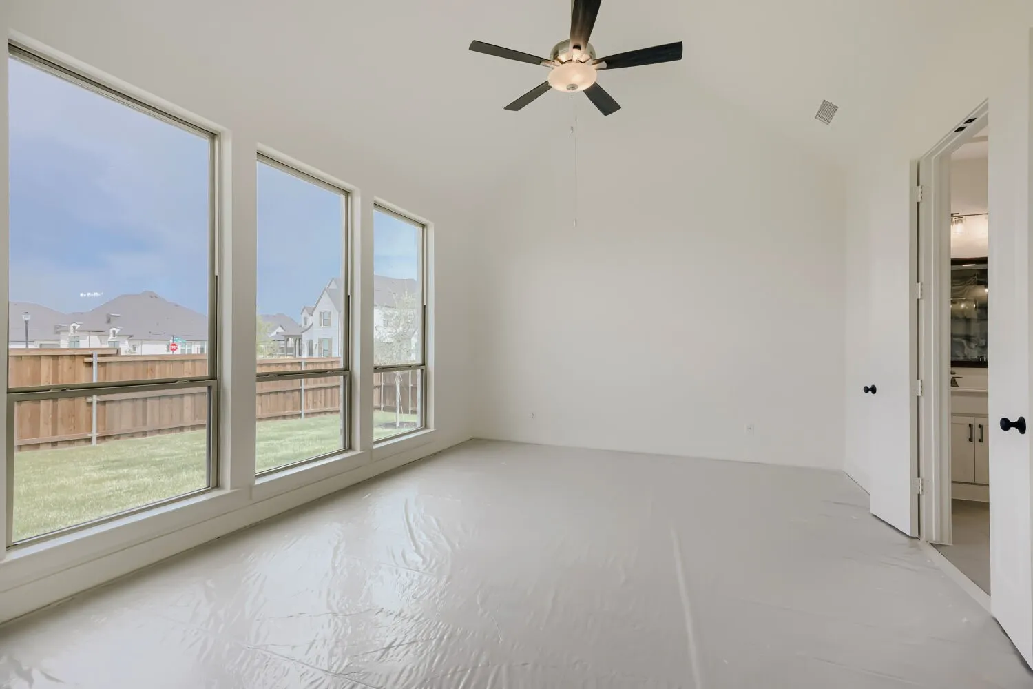 Bright interior space featuring a row of three large windows, a vaulted ceiling with a ceiling fan, and a view of a fenced backyard