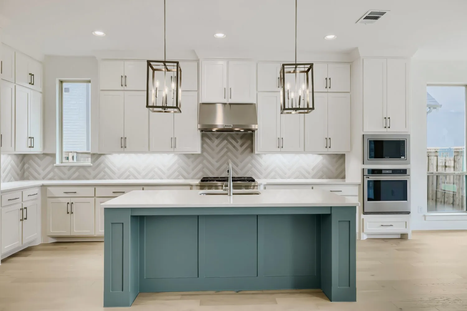 Contemporary kitchen featuring a prominent island with a teal base, white countertops, stainless steel appliances, herringbone tile backsplash, and wood-finish flooring
