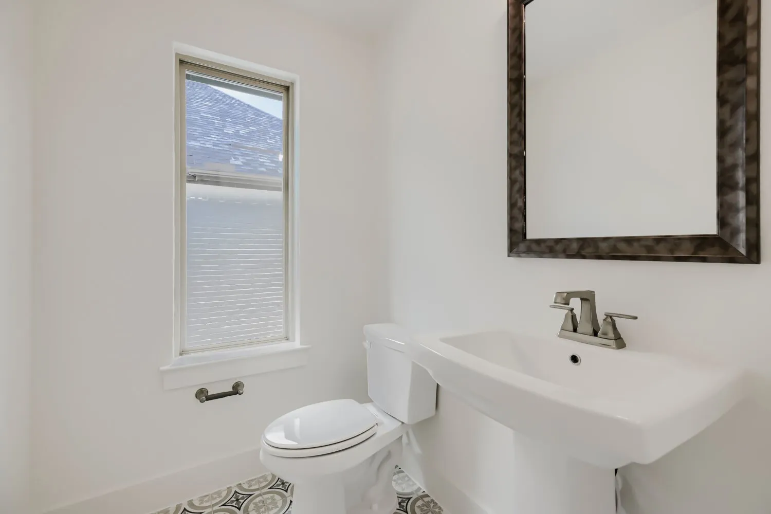 Pedestal sink with a brushed nickel faucet, framed mirror, and a window with blinds