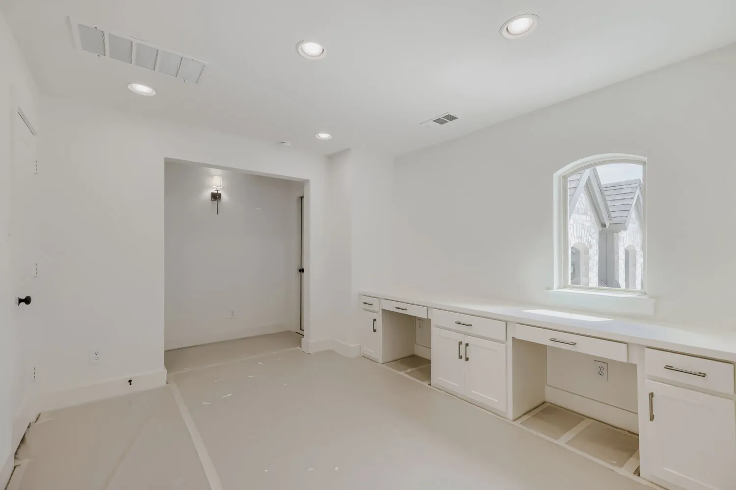 Room featuring built-in white cabinetry, integrated desk spaces, and a curved arch window