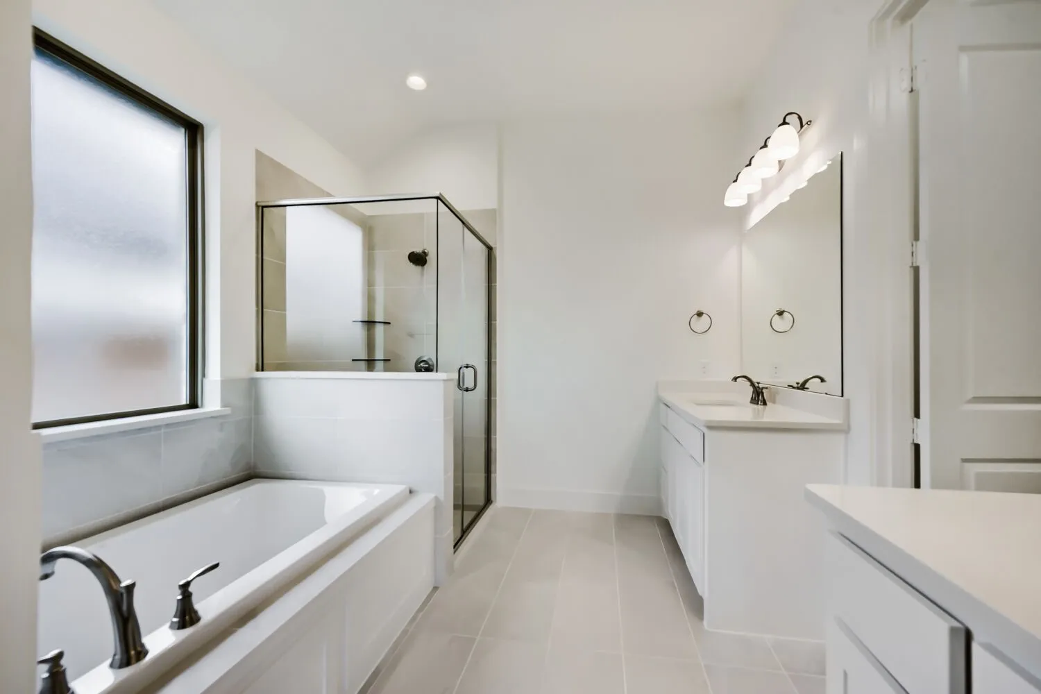 Bathroom featuring a built-in tub, a glass-enclosed shower with tiled walls, dual vanities with integrated sinks, and a large window with frosted glass