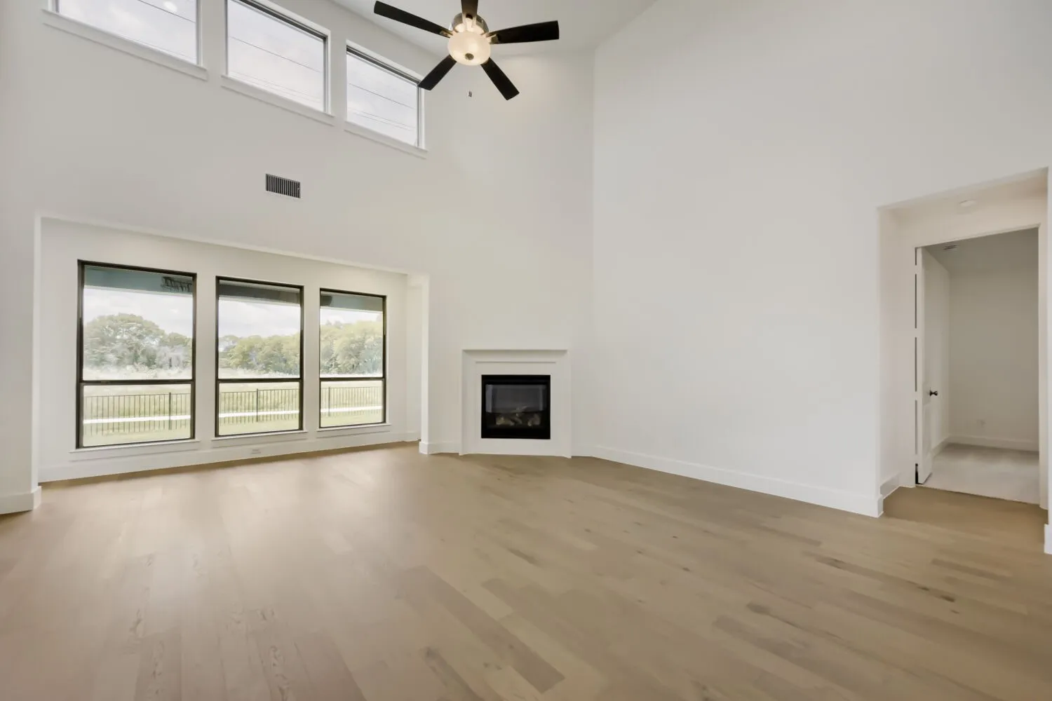 Vaulted living space featuring wood-finish flooring, a corner fireplace, and a ceiling fan