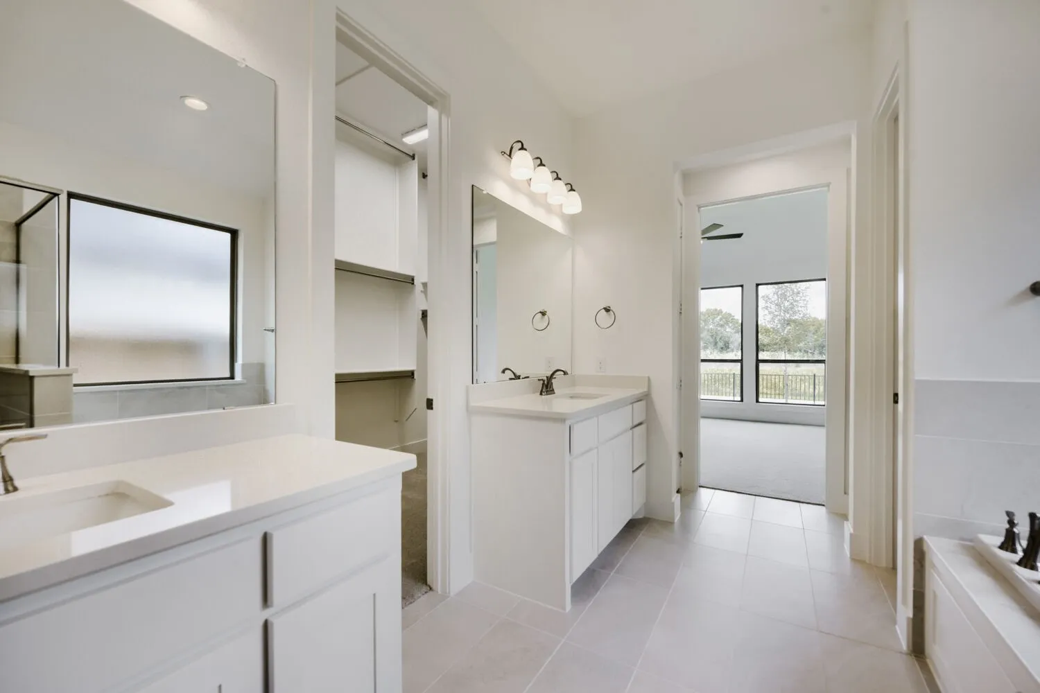 Bright bathroom featuring dual vanity sinks with white cabinetry and light countertops, a walk-in shower with clear glass enclosure, a built-in bathtub, and an adjacent walk-in closet with shelving