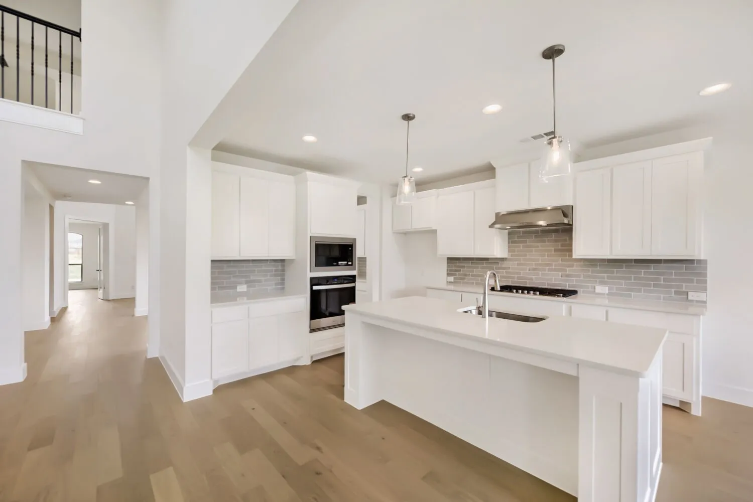 Bright kitchen featuring a central island with an undermount sink, white cabinetry, integrated stainless steel appliances, a subway tile backsplash, and recessed lighting