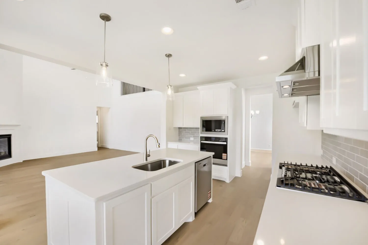Modern kitchen featuring a large island with an undermount sink, stainless steel appliances, white cabinetry, a gas cooktop with a range hood, and light wood-finish flooring