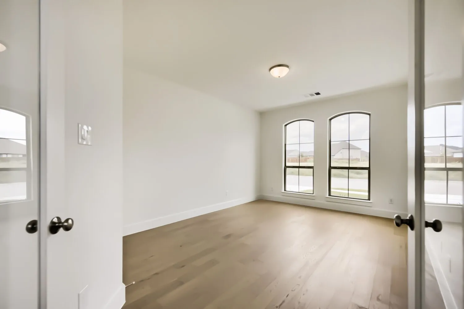 Light-filled room featuring two arched windows, wood-finish flooring, white baseboards, and a semi-flush mount ceiling light