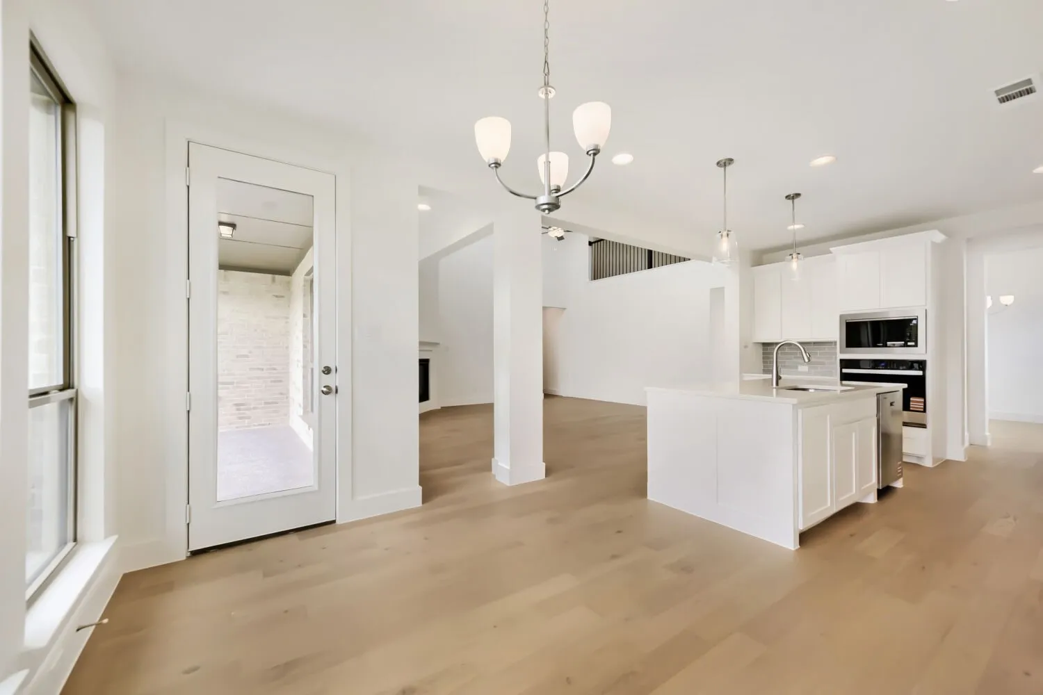 Expansive kitchen and dining area featuring light wood-finish flooring, a contemporary chandelier, recessed lighting, a kitchen island with sink, and stainless steel appliances