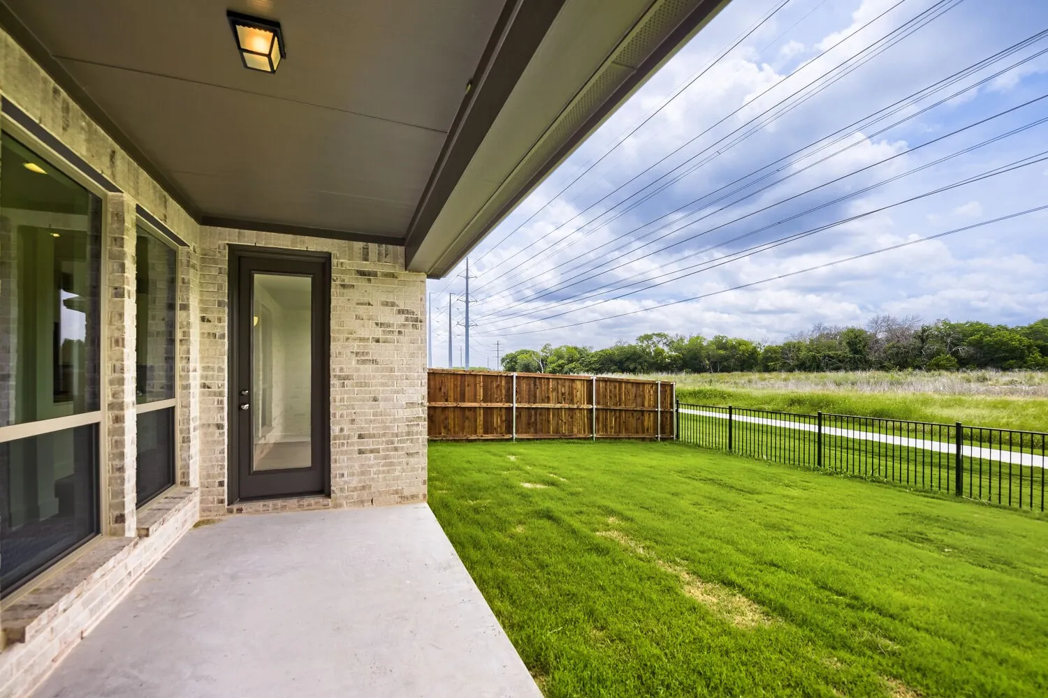 Covered patio with light-toned brick facade, black framed full-light door, and large windows