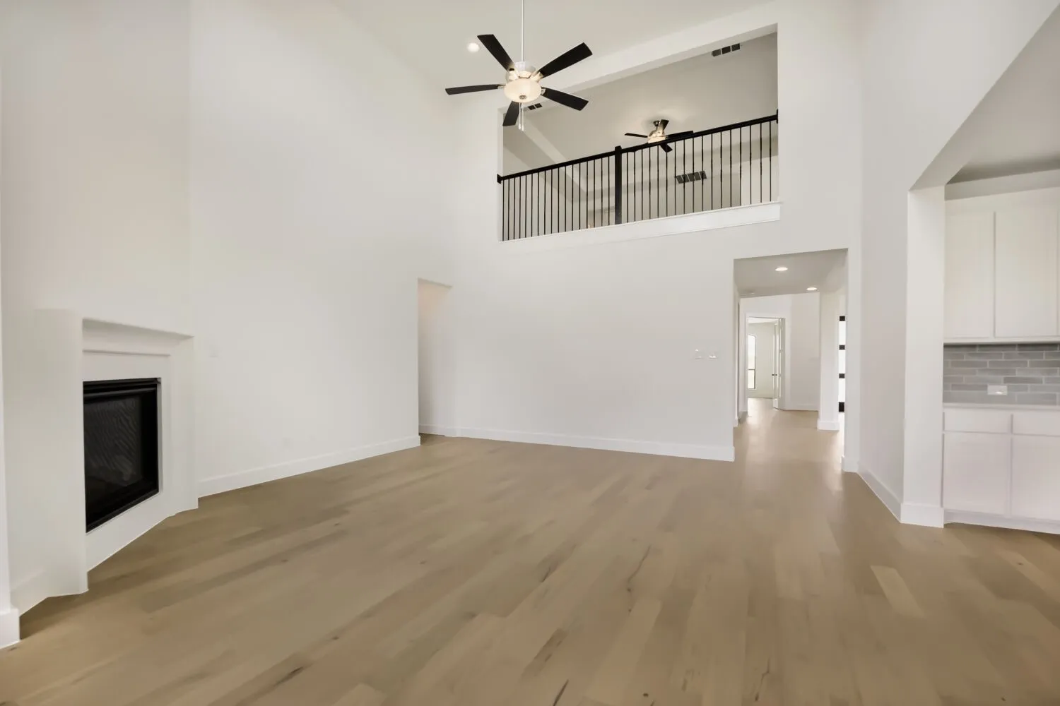 Spacious living area featuring a vaulted ceiling with dual ceiling fans, a built-in fireplace, and light wood-finish flooring