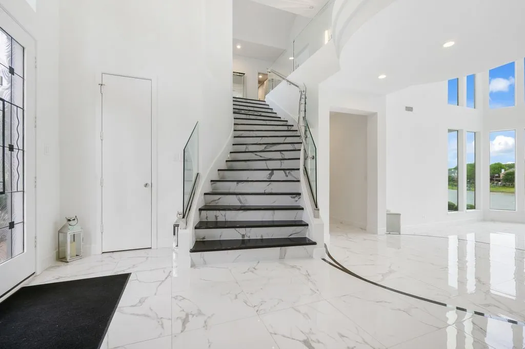 As you enter through the main door, a striking staircase with modern glass railings greets you, a design element that flows seamlessly throughout the home.