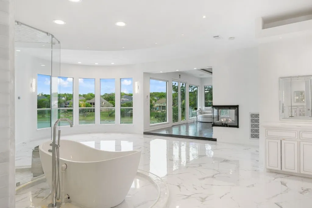 Stunning spa-style primary bath with a freestanding soaking tub and wall of windows framing peaceful lake views for a true retreat experience.