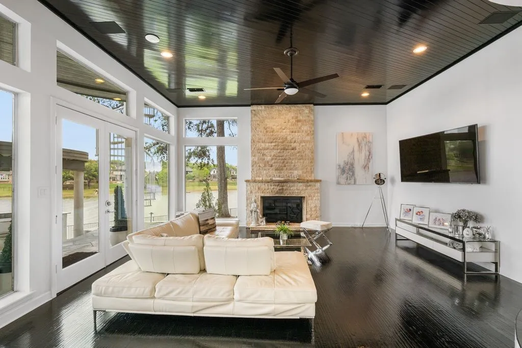 Striking modern design with floor-to-ceiling windows flooding the living area with natural light. The sleek dark ceiling, paired with rich wood flooring and a stone fireplace, creates a warm yet sophisticated atmosphere. A perfect blend of contemporary style and comfort.