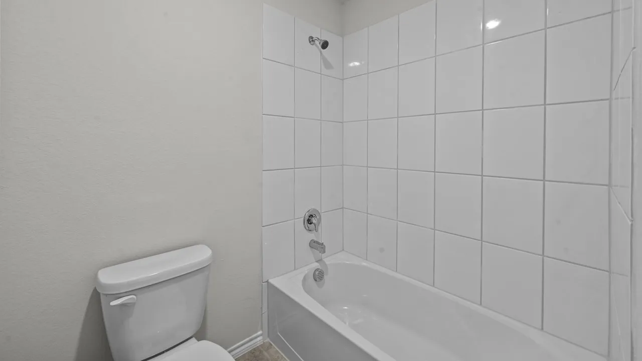 Full bathroom featuring a white porcelain toilet, white subway tile shower surround, chrome shower fixtures, and white tub