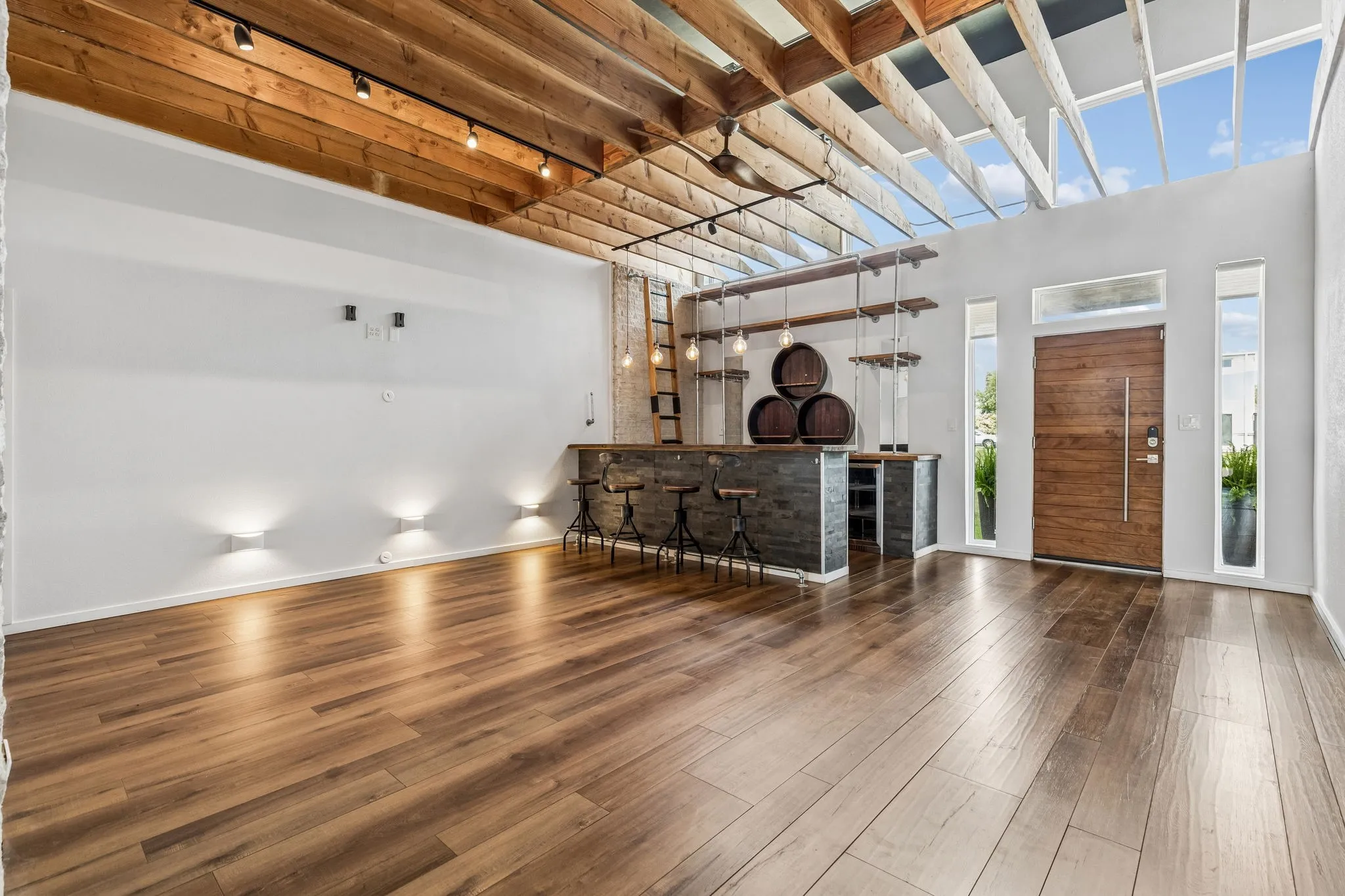 View of solid wood front door, bar and wood flooring in first living area.