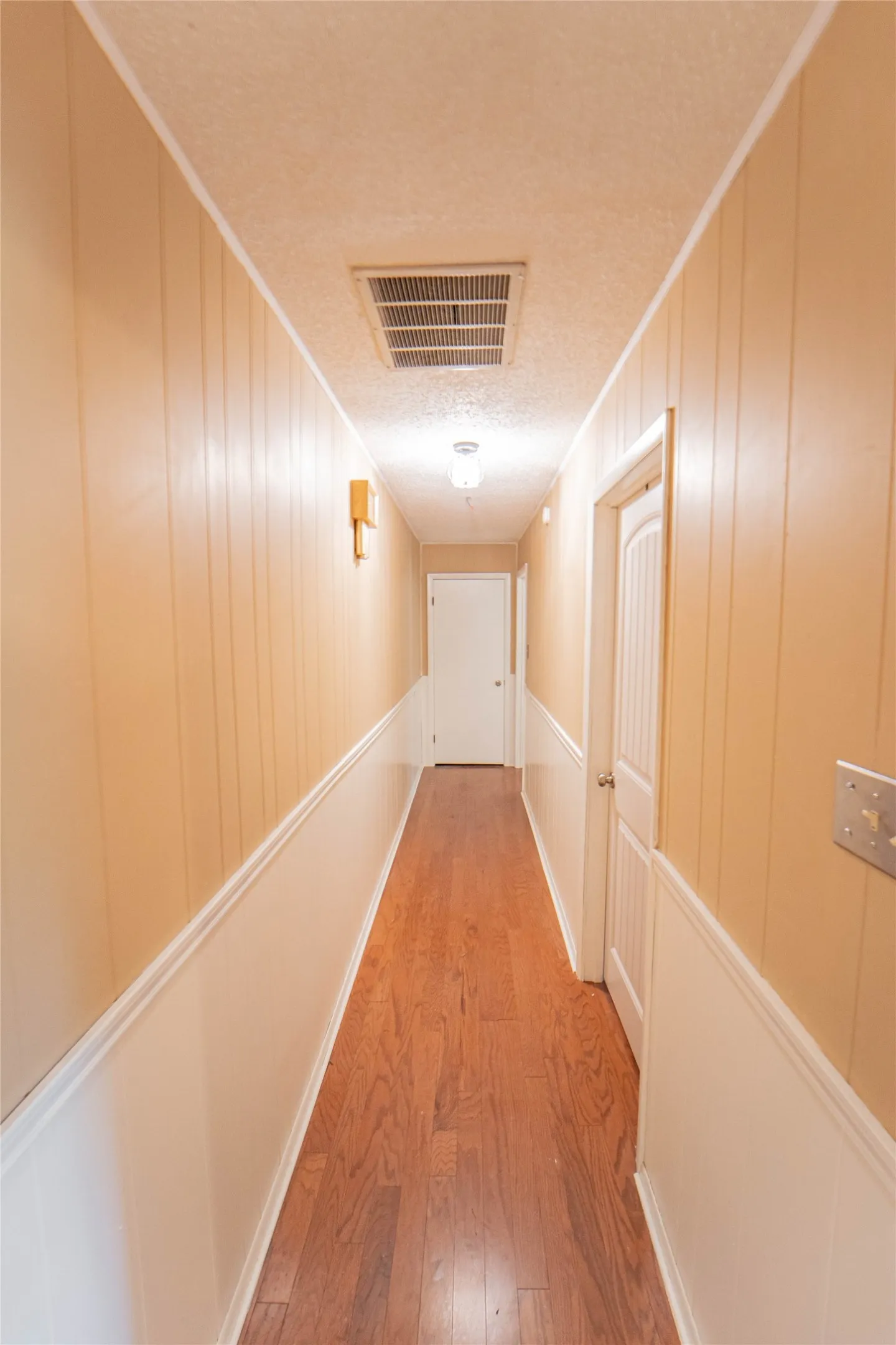 Corridor featuring light wood-type flooring, a textured ceiling, and wood walls