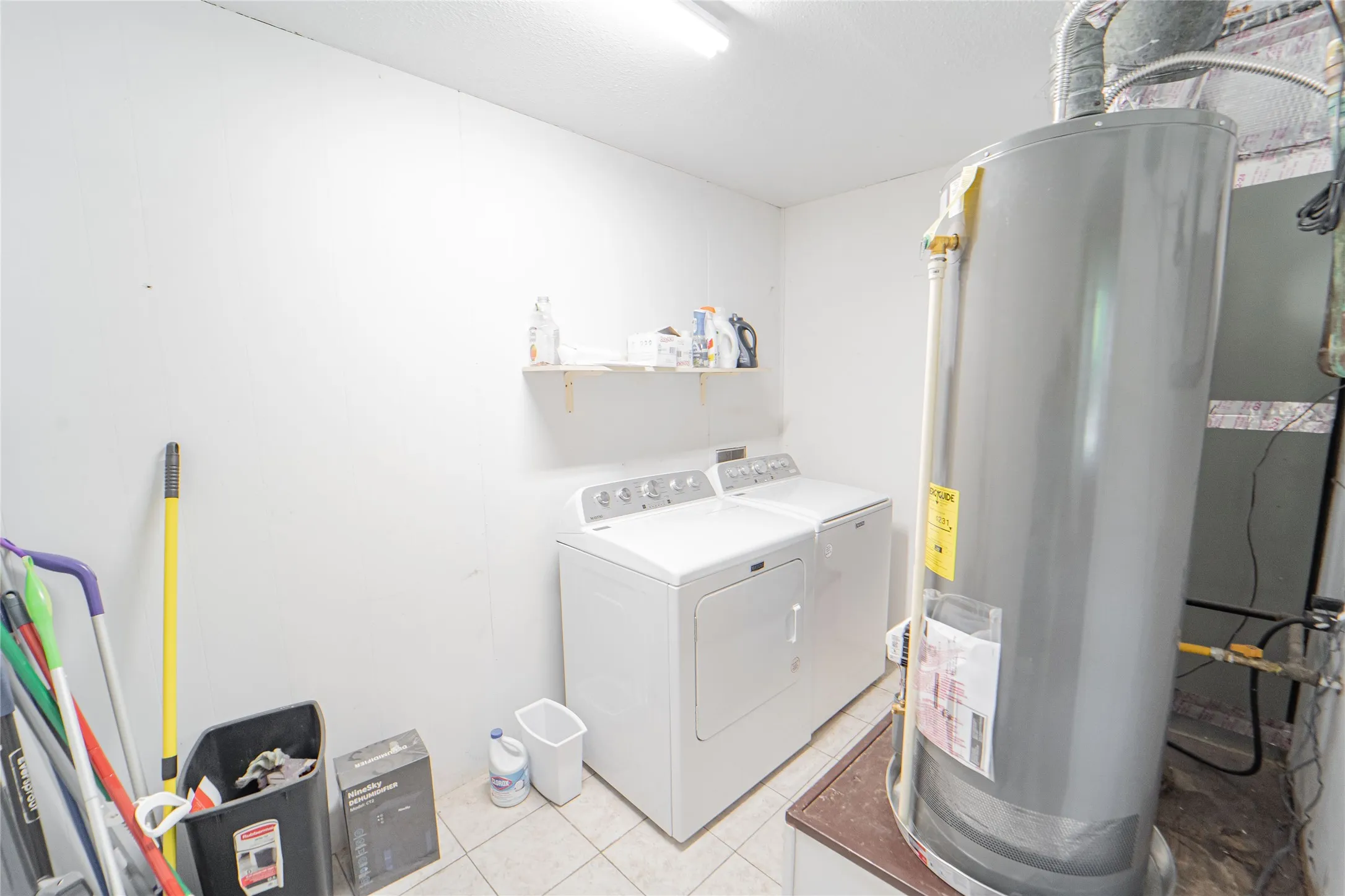 Laundry room with water heater, washer and dryer, and light tile patterned floors