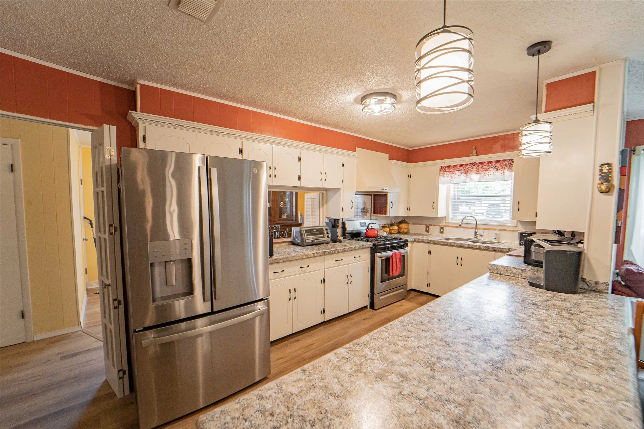 Kitchen featuring stainless steel appliances, light countertops, light wood finished floors, a textured ceiling, and pendant lighting