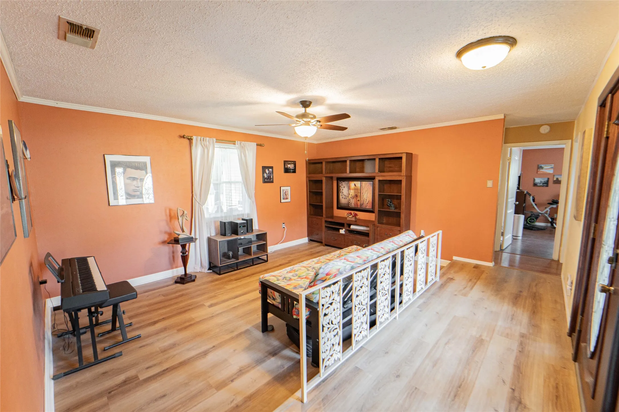 Living area featuring light wood-style floors, ceiling fan, ornamental molding, and a textured ceiling