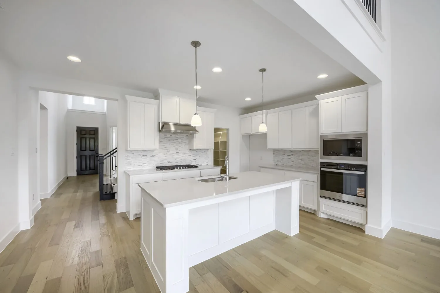 Open-concept kitchen featuring an island with a sink, stainless steel appliances, white cabinetry, a tiled backsplash, and wood-finish flooring