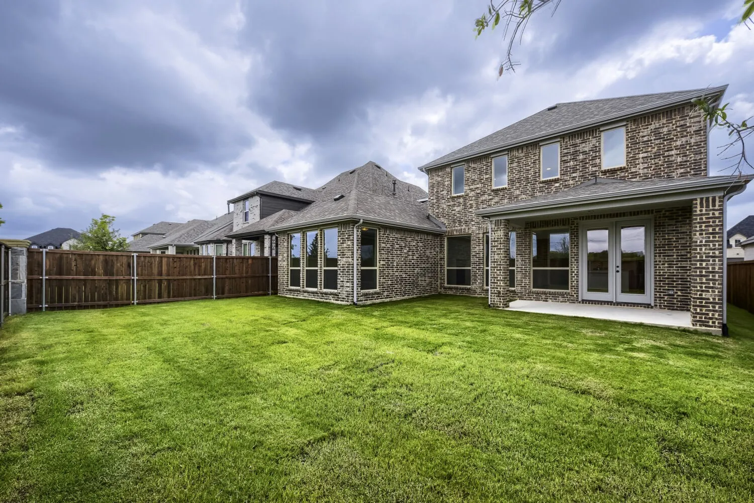 Expansive backyard featuring a manicured lawn, full privacy fencing, and a covered patio