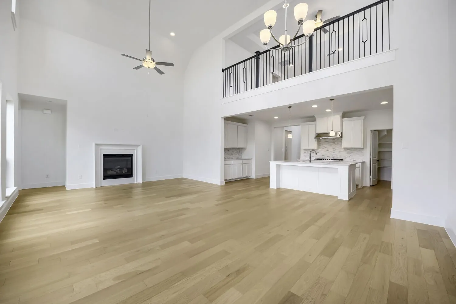 Open-concept living space featuring wood-finish flooring, a two-story ceiling, and a fireplace with a white mantel