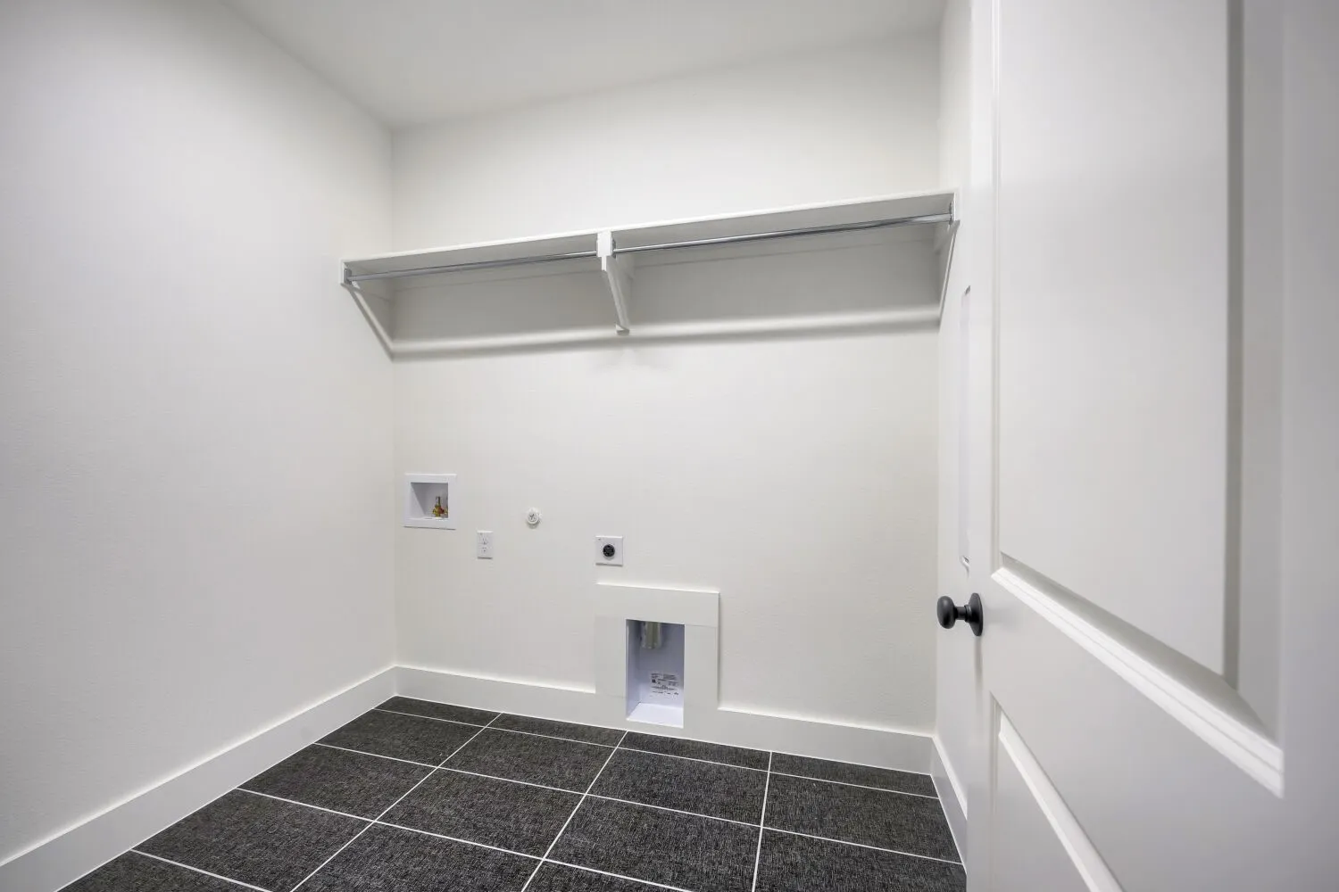 Dedicated laundry area featuring dark tile flooring, white walls, and a built-in shelving system