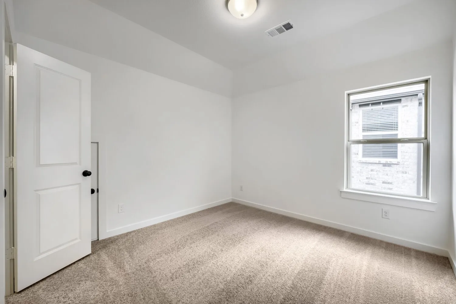 Carpeted room featuring a single window with blinds, white trim, and a white interior door with black hardware