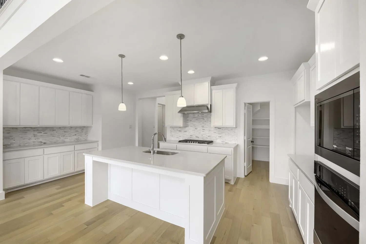 Spacious kitchen featuring an expansive central island, white cabinetry, integrated stainless steel appliances, a tile backsplash, and light wood-finish flooring