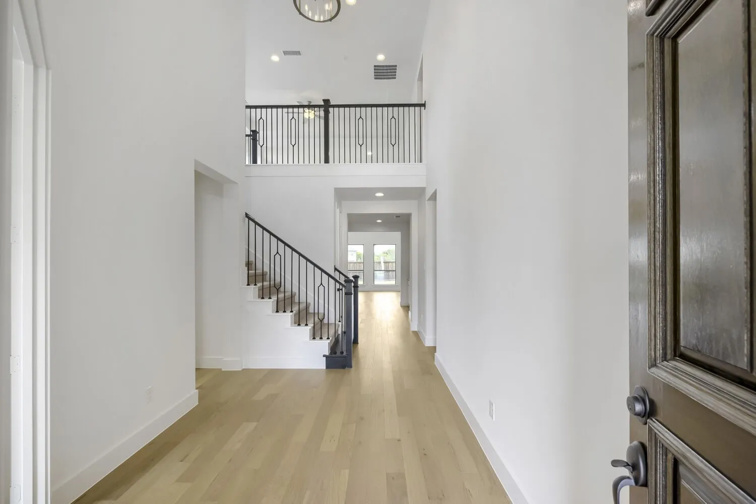 Foyer featuring a grand two-story ceiling, light wood-finish flooring, and a staircase with decorative wrought iron spindles
