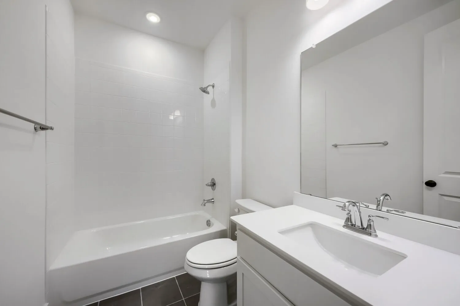 Bathroom featuring a white subway tile tub surround, dark tile flooring, a white vanity with a rectangular sink, a large vanity mirror, and recessed lighting