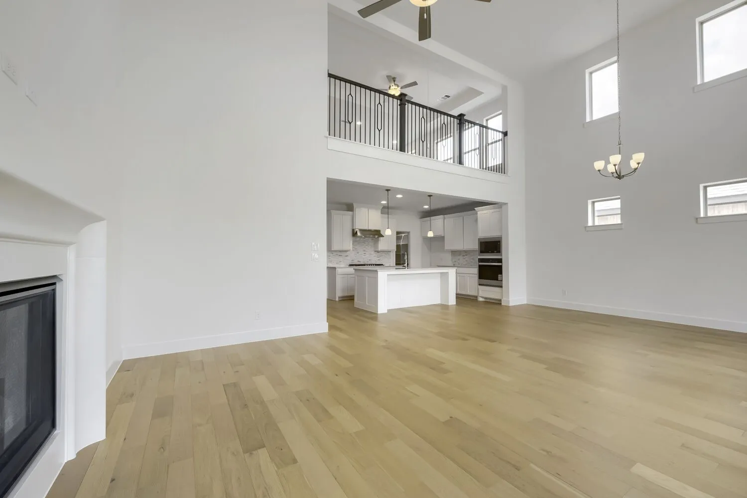 Spacious living area featuring high ceilings, wood-finish flooring, and a fireplace with a white mantel