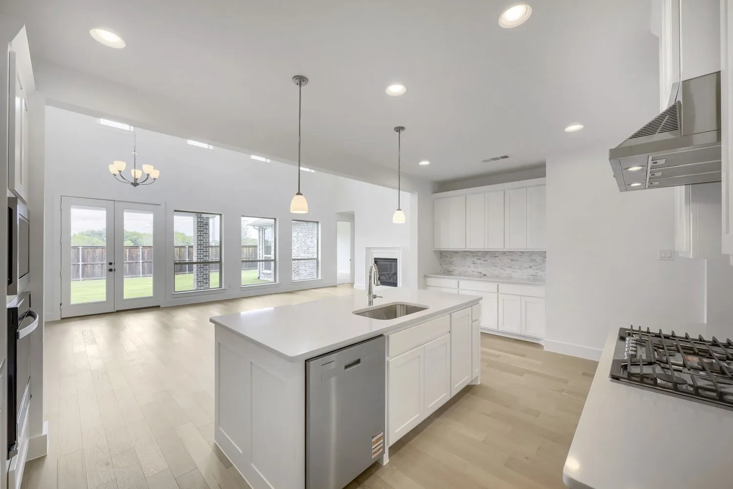 Open-concept kitchen featuring an island with a stainless steel sink and dishwasher, white cabinetry, a gas cooktop with a stainless steel range hood, and light wood-finish flooring