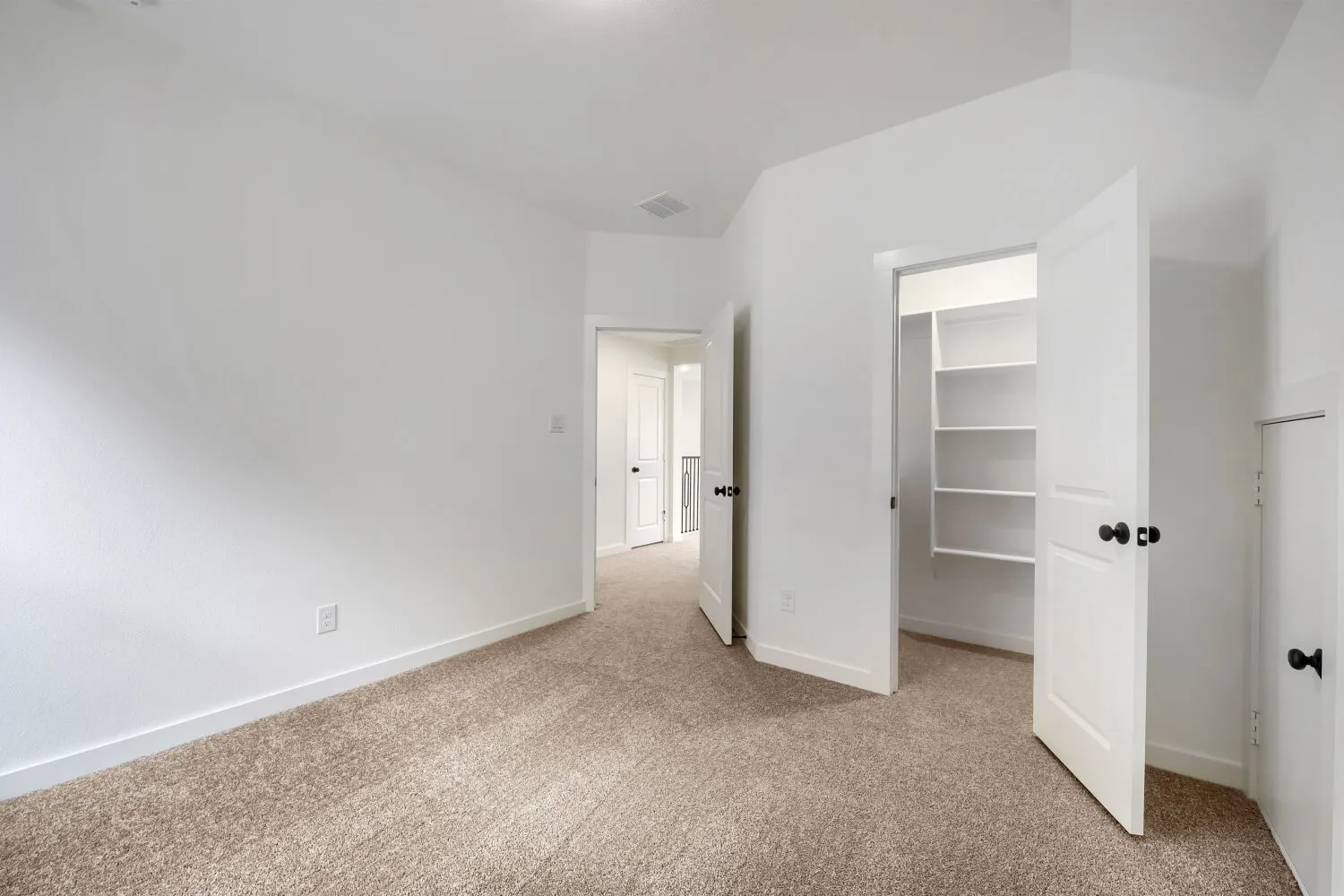 Carpeted room featuring a double-door closet with built-in shelving, white baseboards, and a neutral color palette