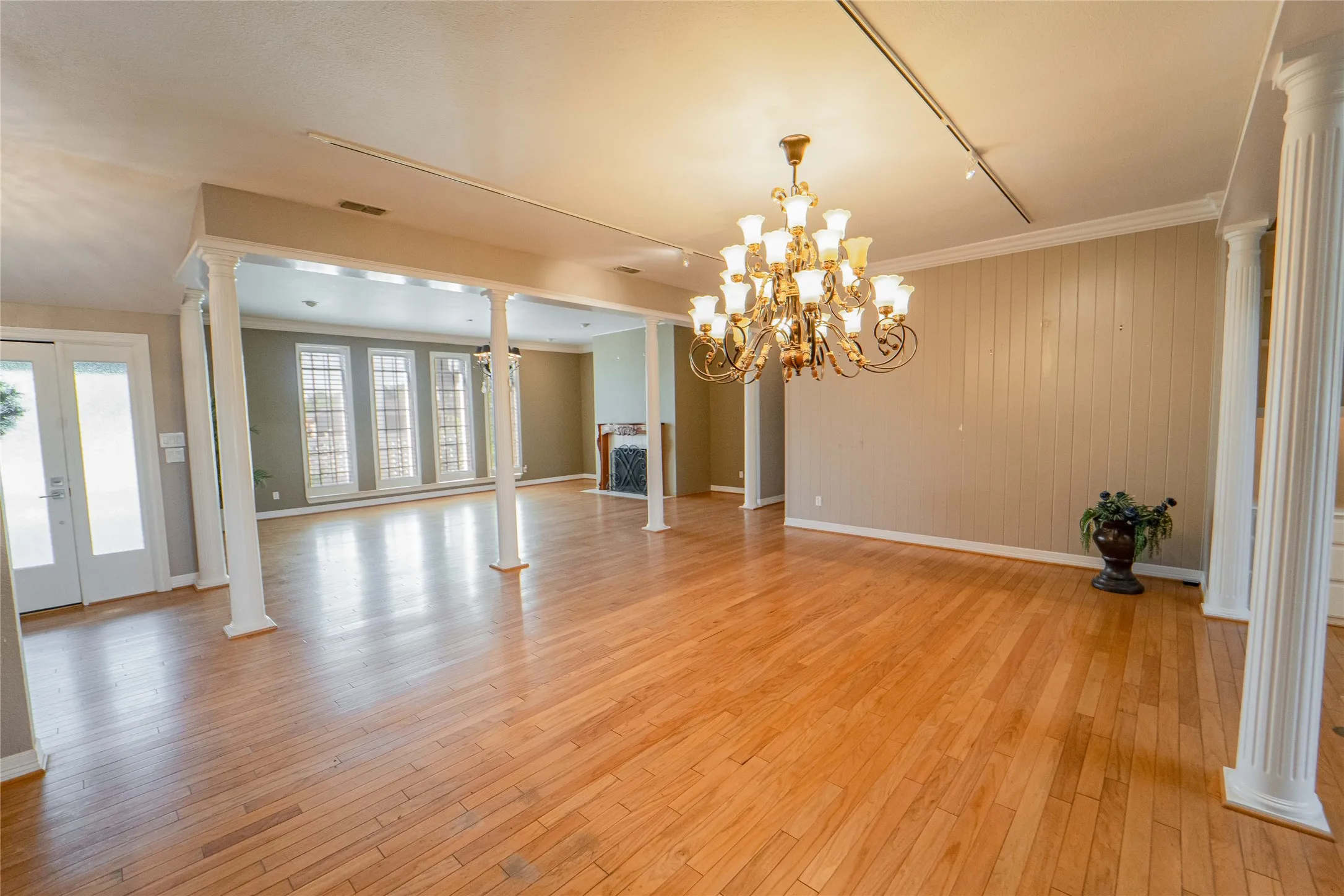 Unfurnished dining area with decorative columns, light wood-type flooring, french doors, a chandelier, and wood walls