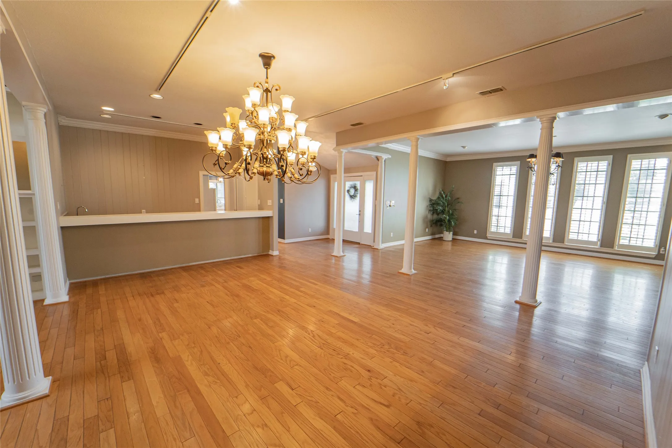 Unfurnished dining area with ornate columns, ornamental molding, light wood finished floors, and suspended lighting