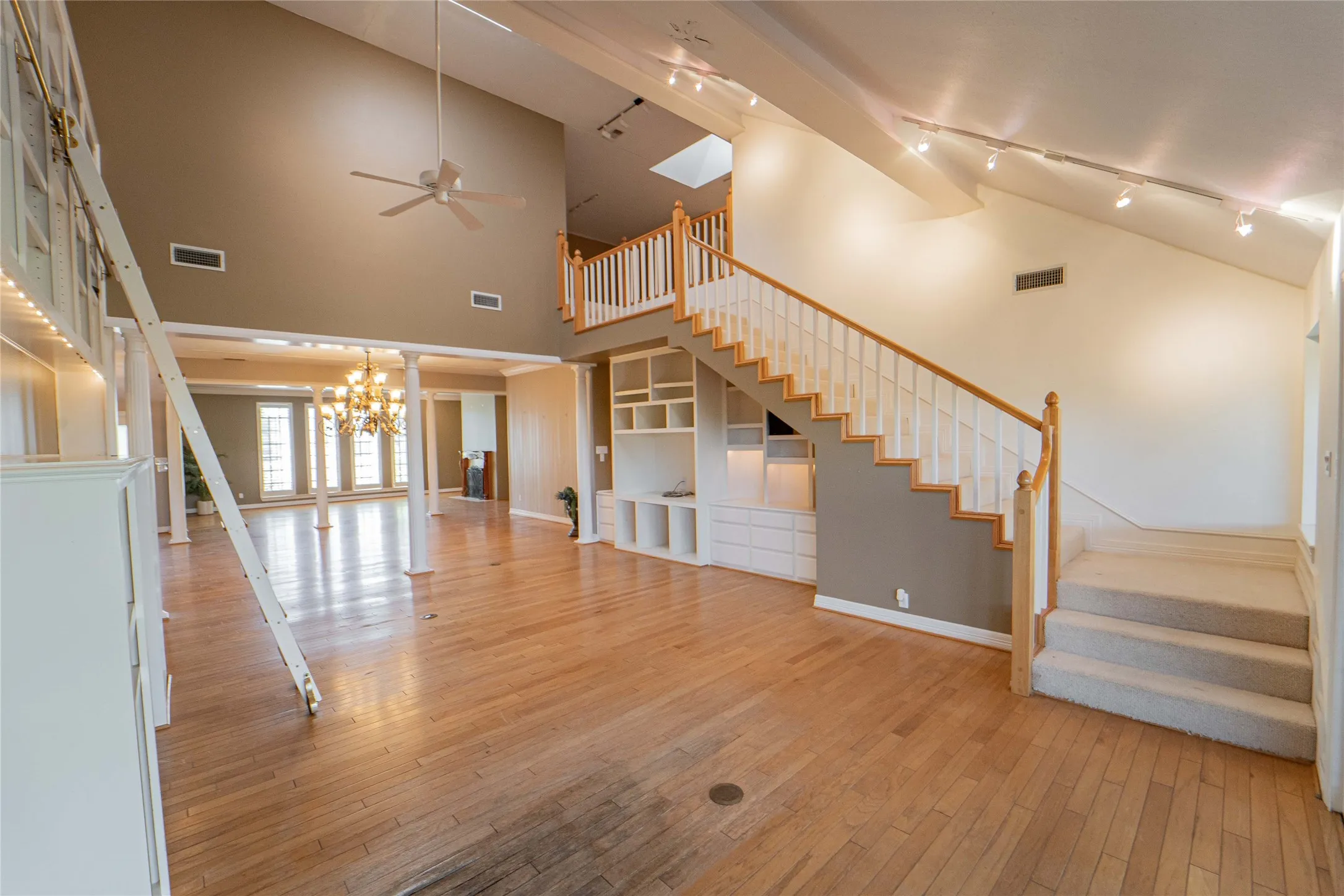 Family room featuring lofted ceiling, light wood-style floors, built in shelves, ceiling fan, and hanging lights