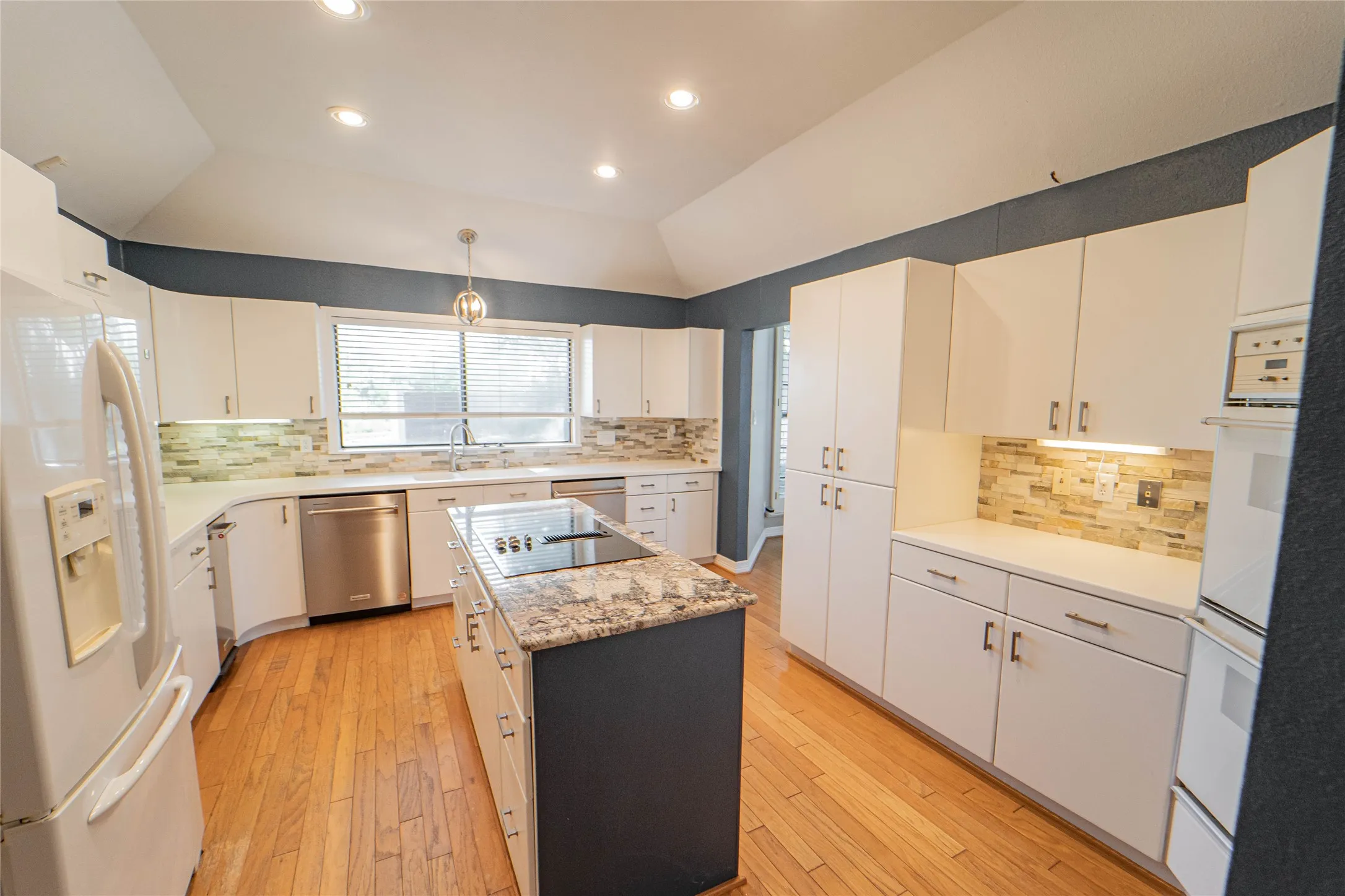 Kitchen with white appliances, tasteful backsplash, light wood-style flooring, lofted ceiling, and white cabinetry
